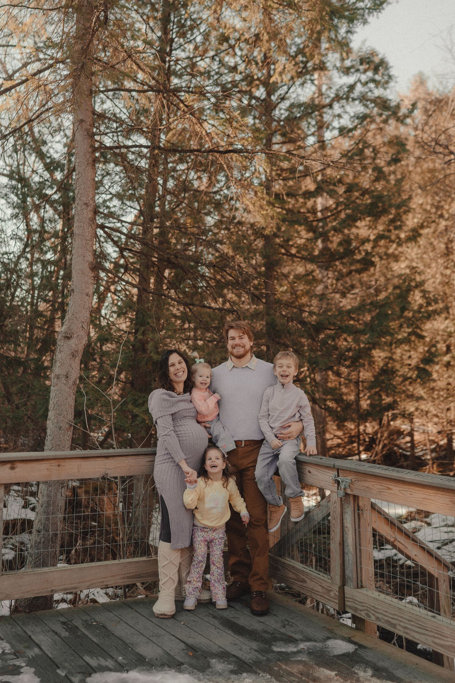 Family portrait series on a wooden deck surrounded by autumn pine trees at sunset.