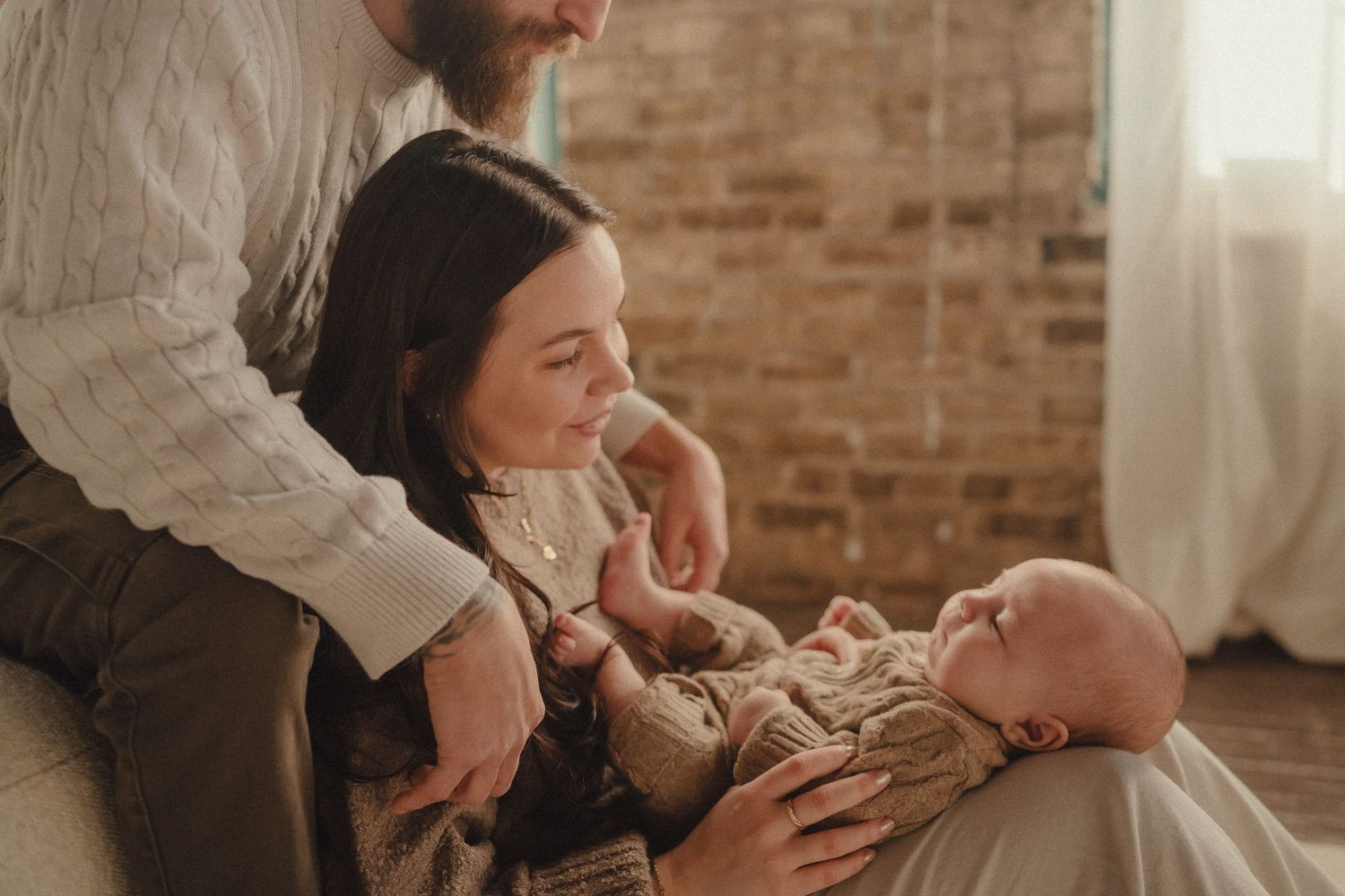 Intimate family moment captured on a beige couch against exposed brick wall.