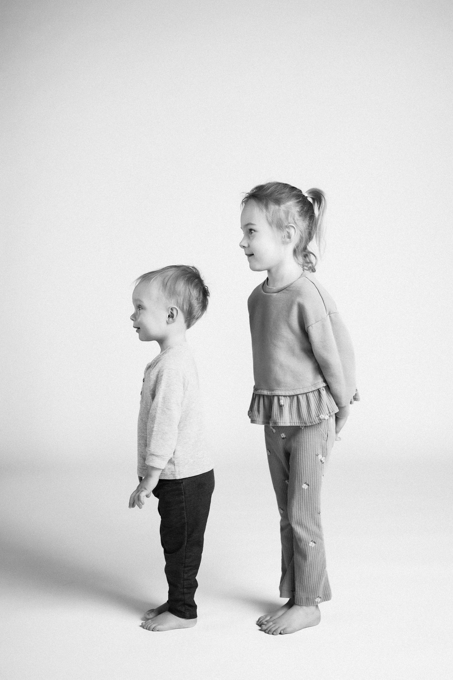 Two small children standing together in profile view against a white background.