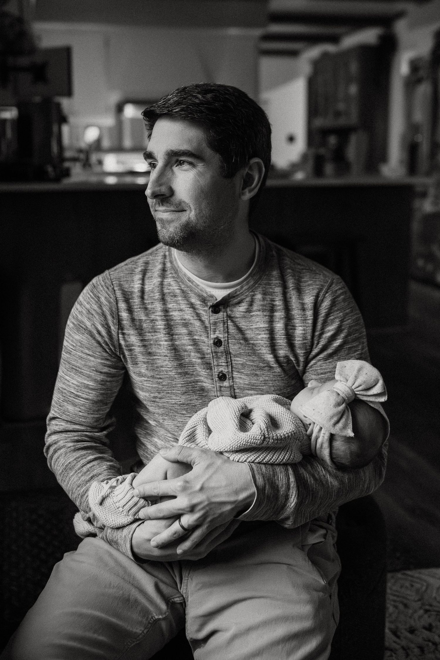 Parent in striped sweater gently cradling sleeping newborn in moody black and white photography.