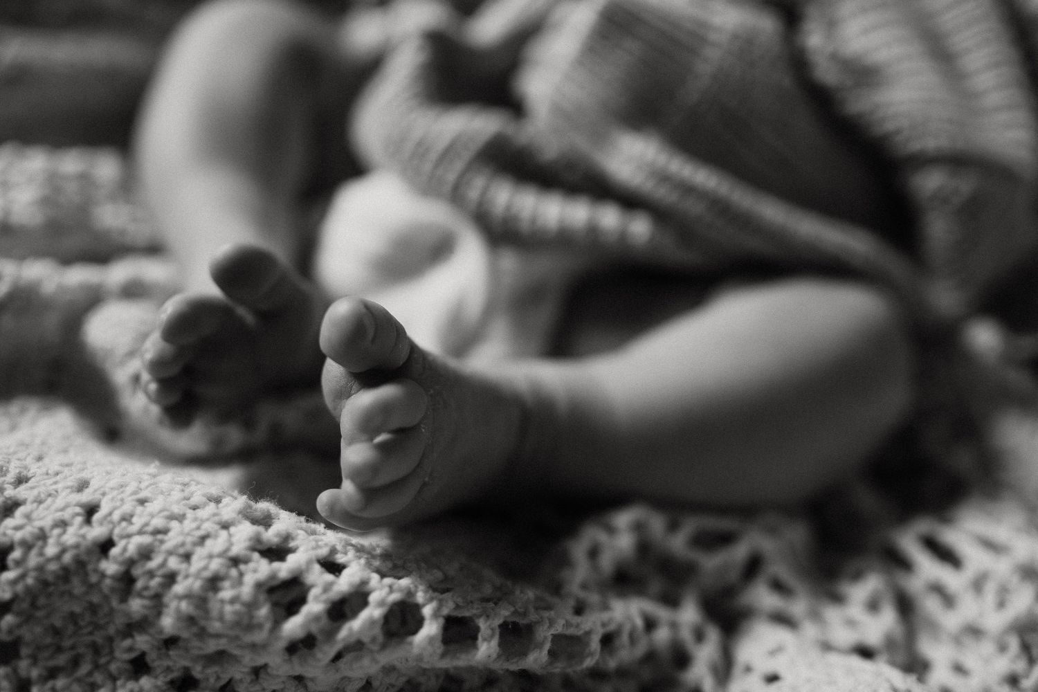 Close-up black and white detail of tiny baby toes against soft textured background.