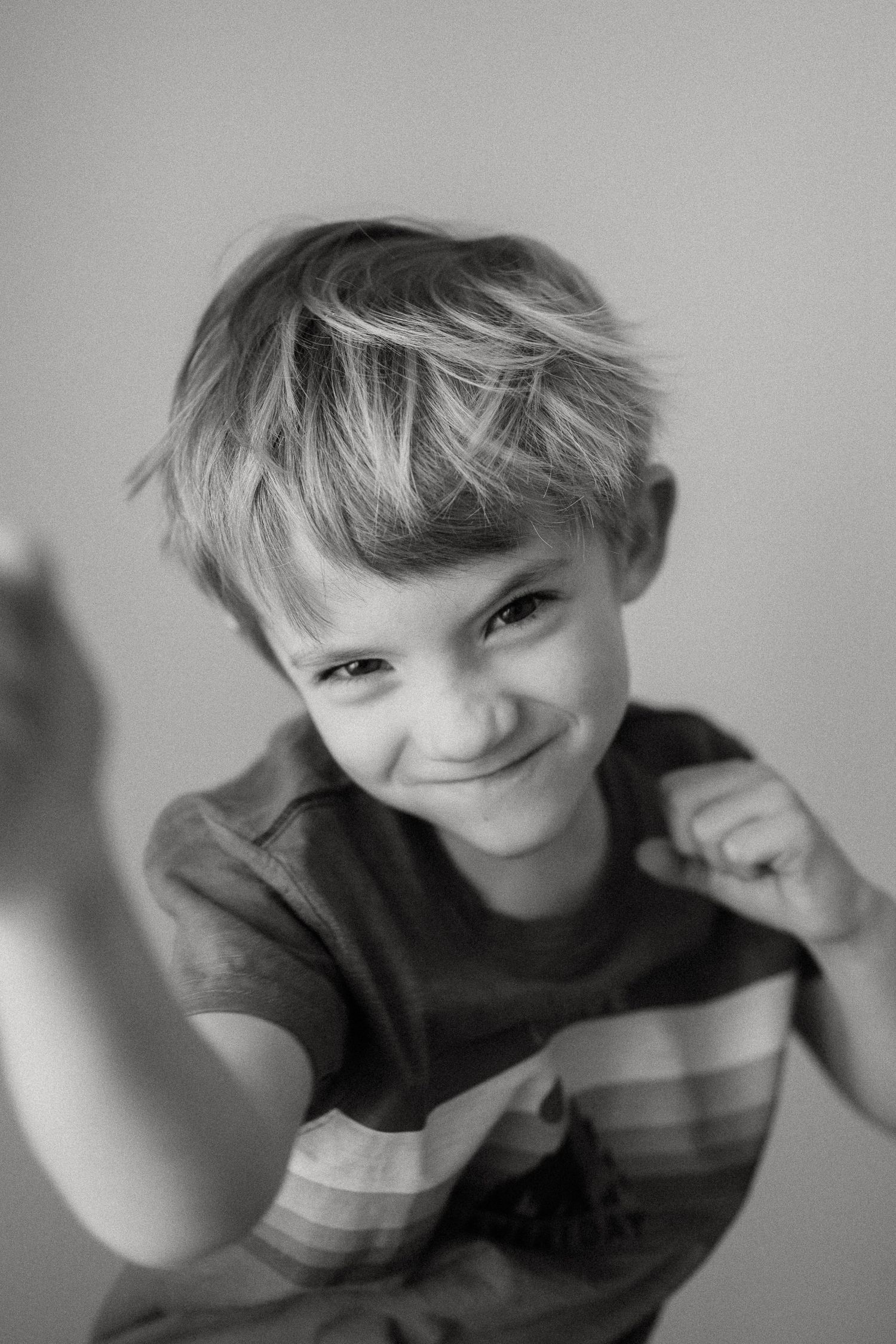 Black and white portrait of a young child in a striped shirt smiling playfully at the camera.