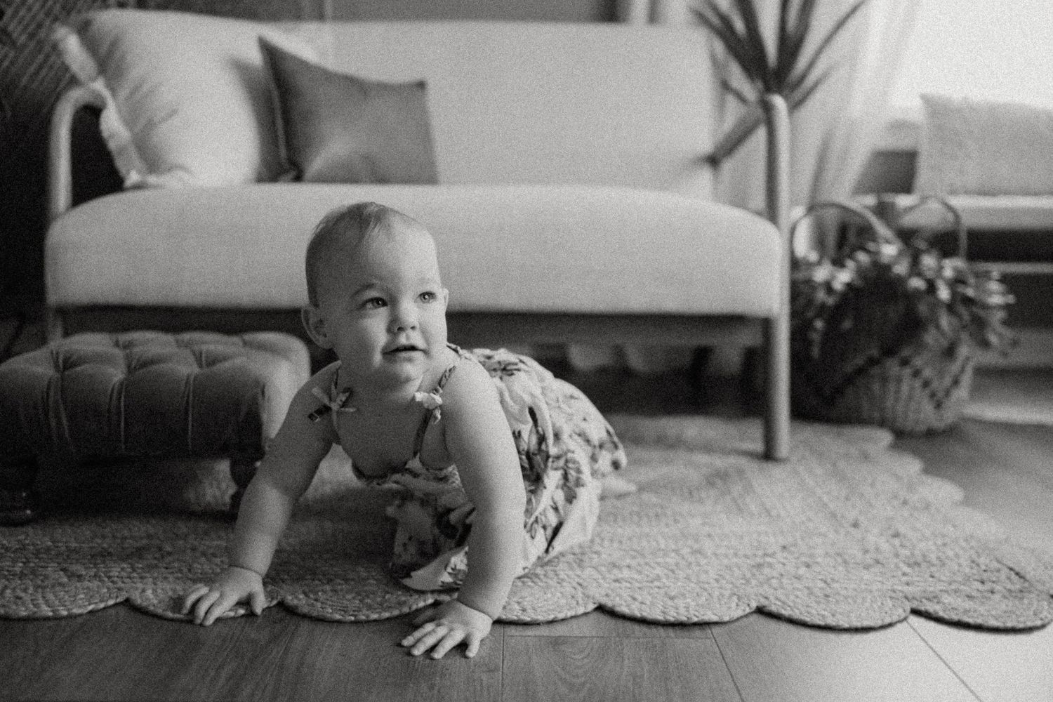 A black and white photo of a toddler crawling on a patterned rug.
