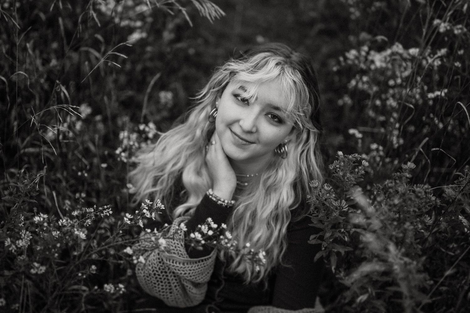 Black and white portrait amidst flowering plants with soft natural lighting.