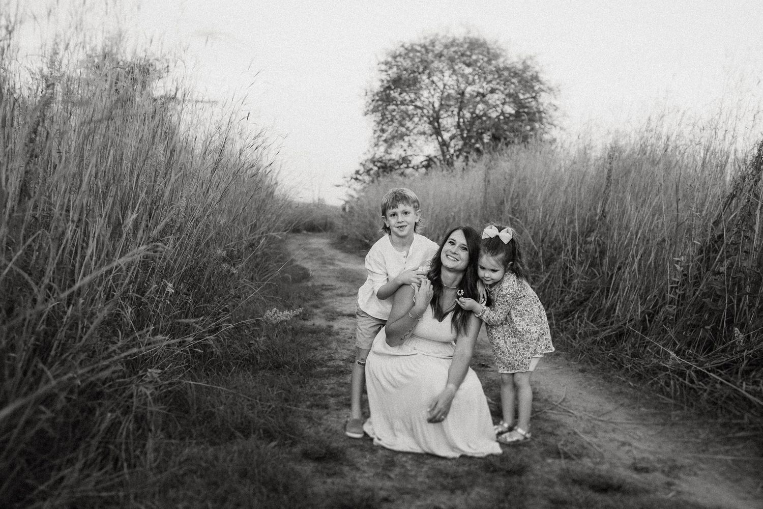 Black and white image of group embracing on nature path surrounded by tall grass.