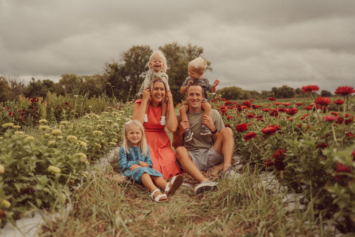 Casual family portrait session in a garden with red flowers under cloudy skies.