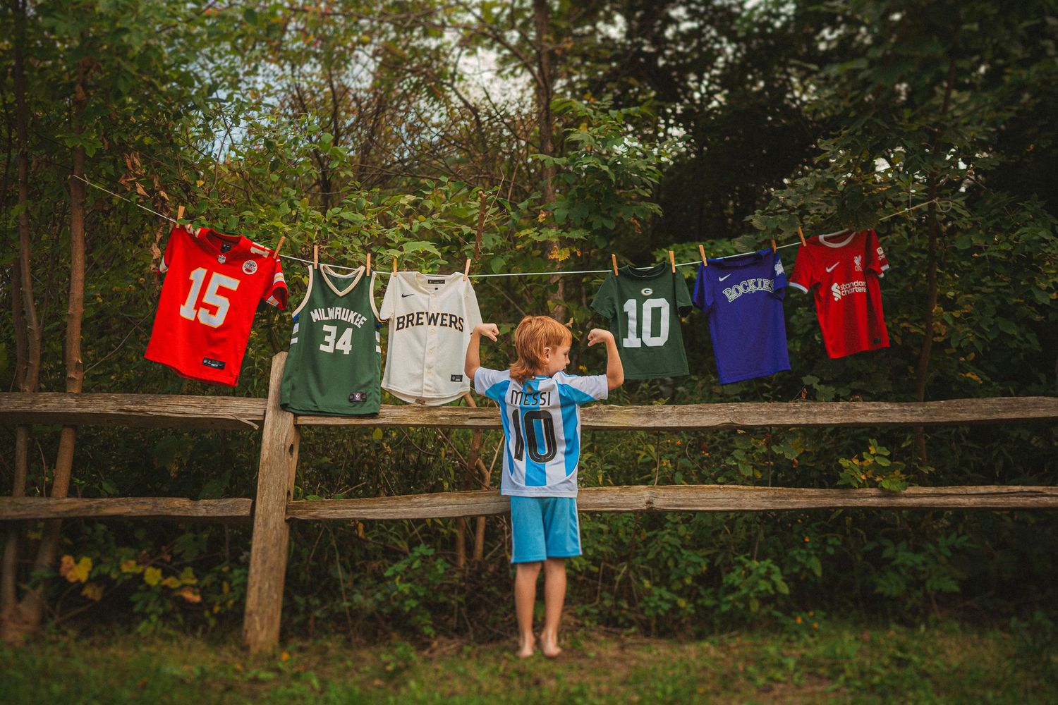 Sports jerseys hanging on a rustic wooden fence with child standing in the middle.