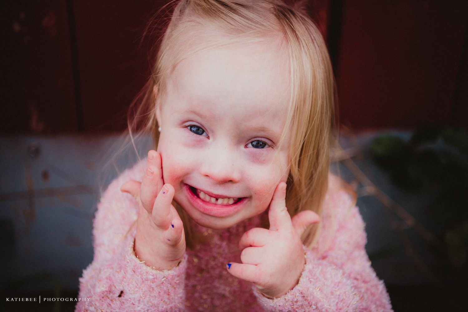 Close-up portrait of a child in pink giving thumbs up with a bright smile.