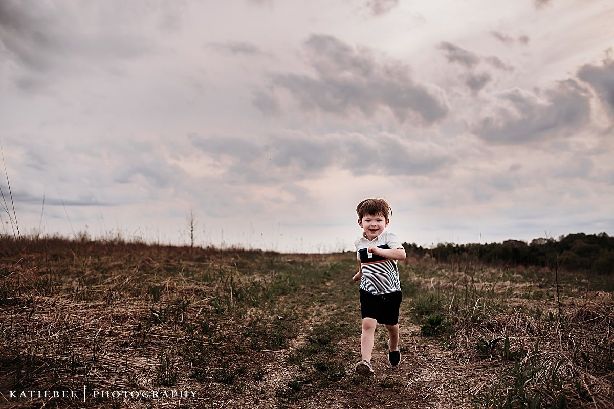 A young child runs along a natural path under stormy skies.