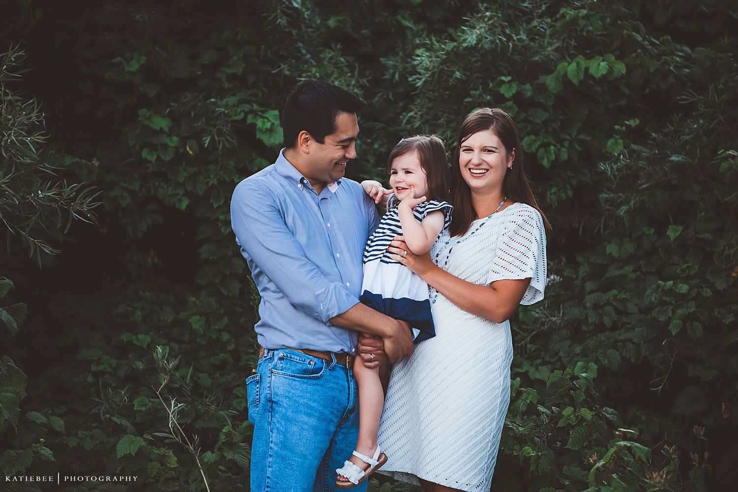 A loving outdoor family portrait captured against green foliage.