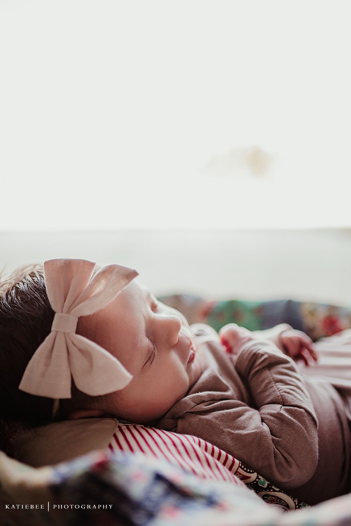 Side profile of sleeping infant with pink bow against soft white background.