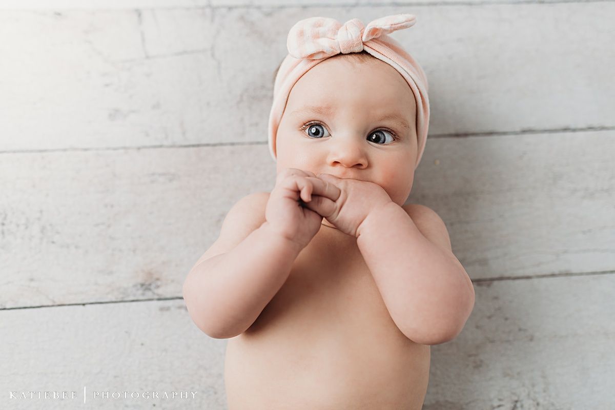 Baby wearing pink headband against white wooden background during portrait session.