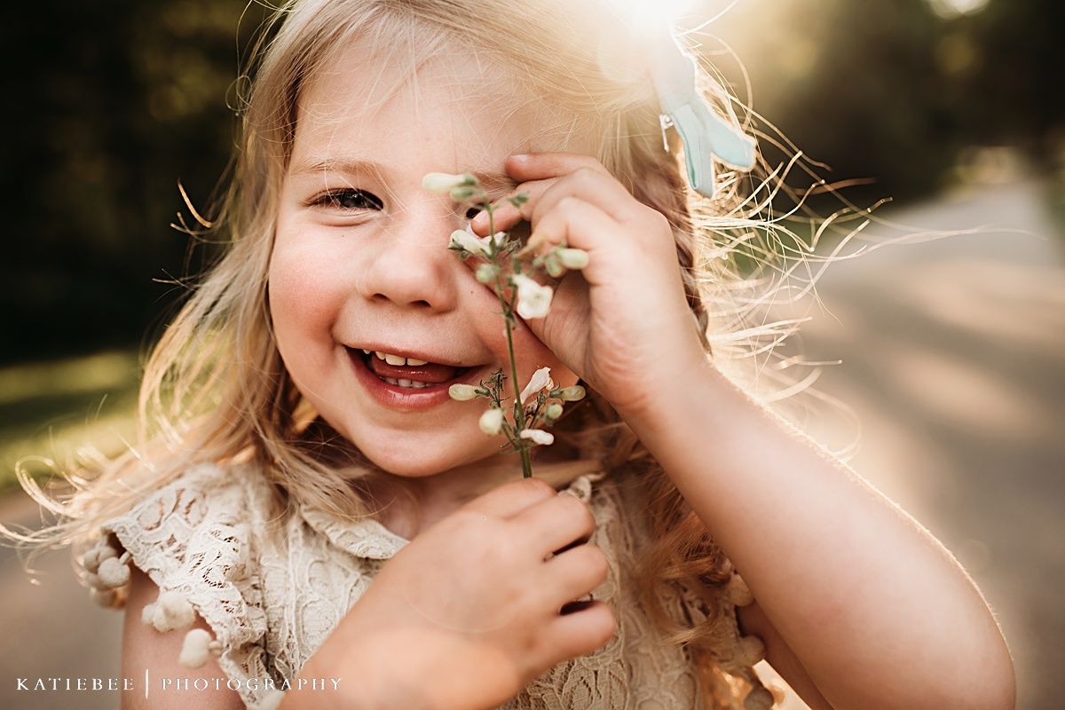 Close-up portrait of joyful child laughing while playing with flowers.