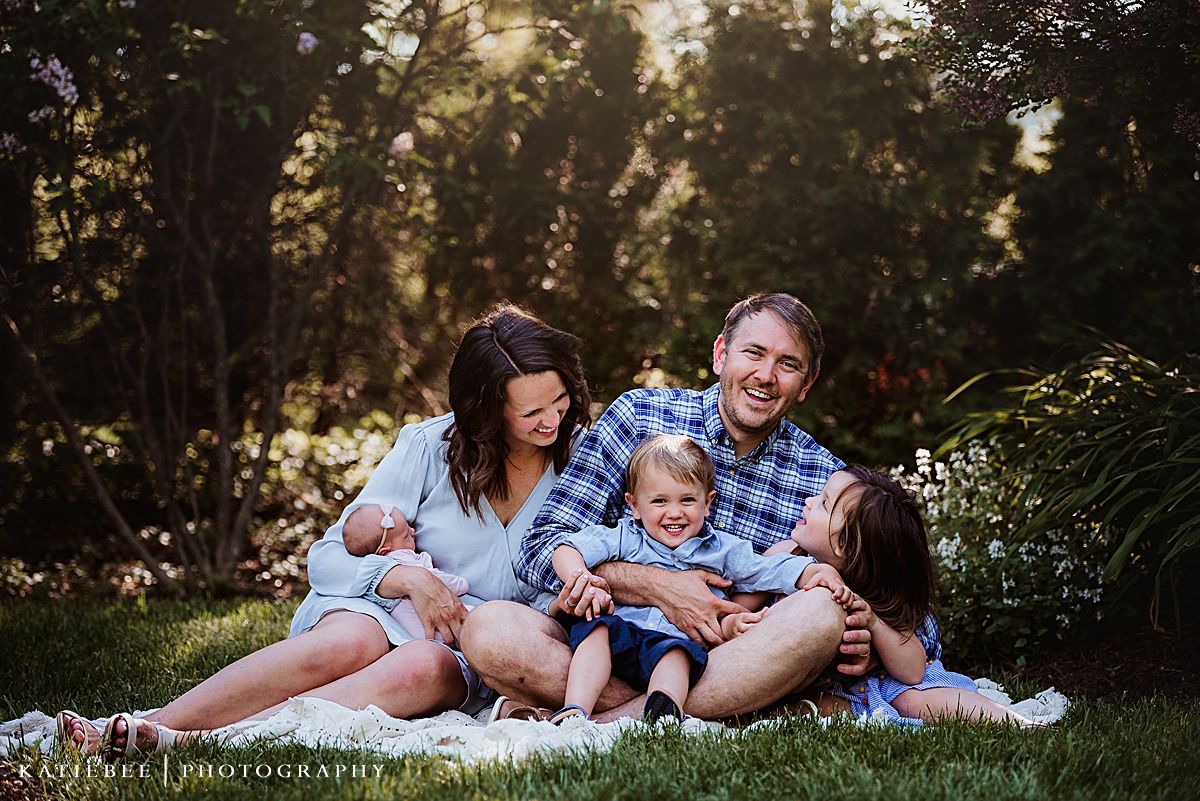 Family portrait on a blanket surrounded by lush garden greenery at sunset.