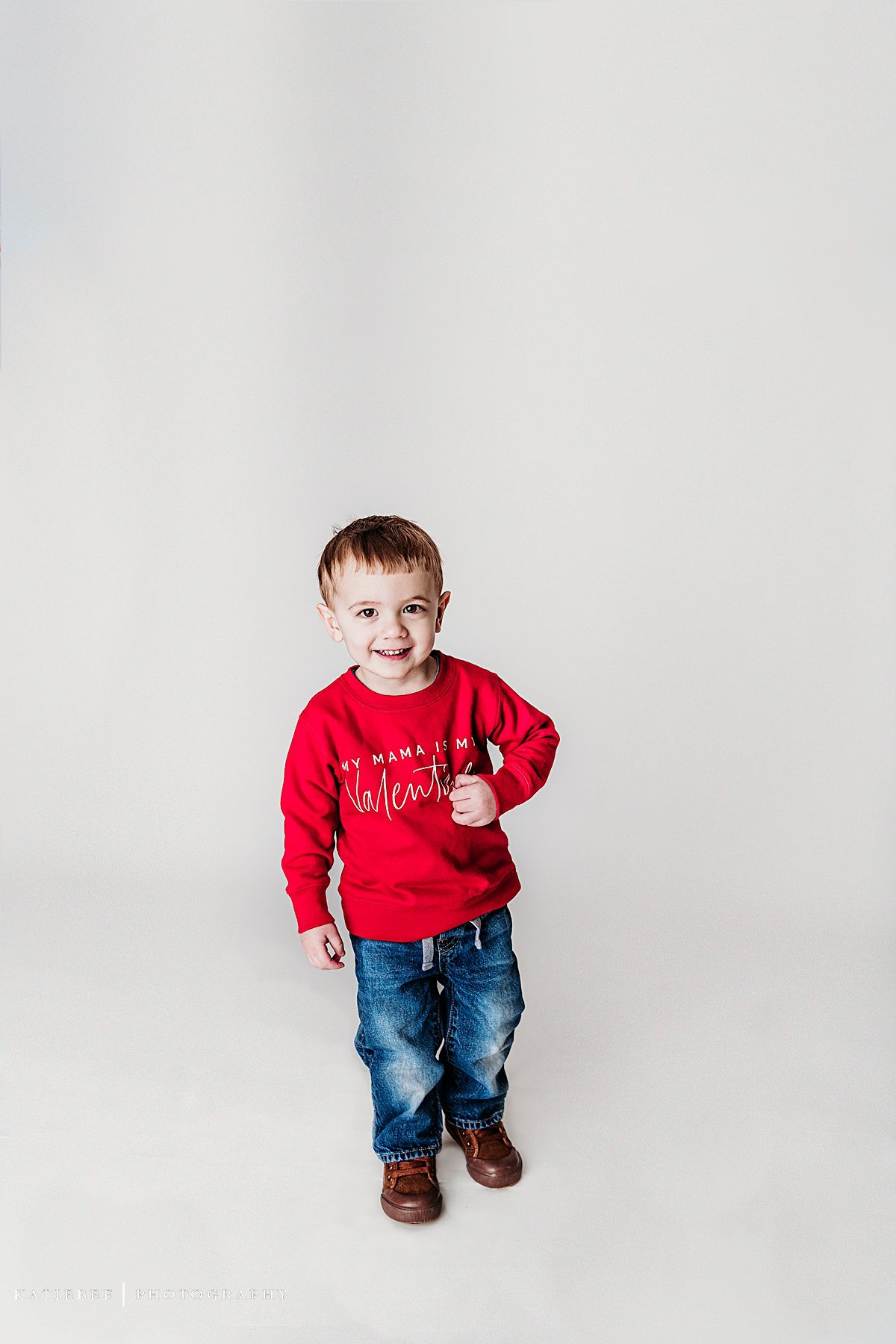 Standing pose against white backdrop in red valentine sweater and distressed jeans.