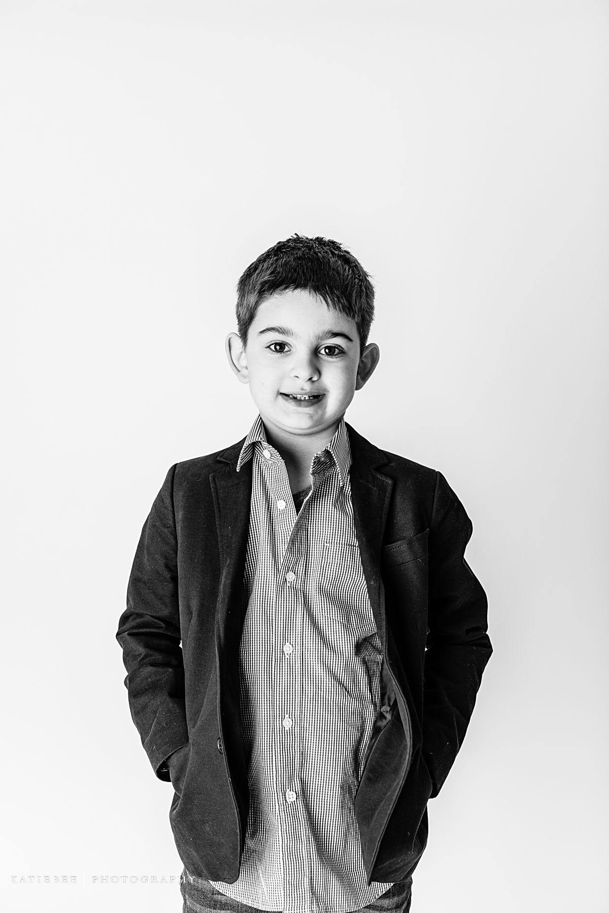 Black and white portrait of a child in dark blazer and striped shirt with hands in pockets.