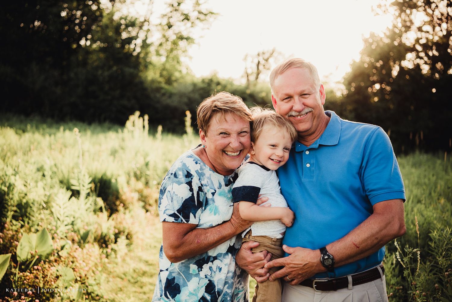 A loving multi-generational family portrait captured in a sunlit meadow during golden hour.