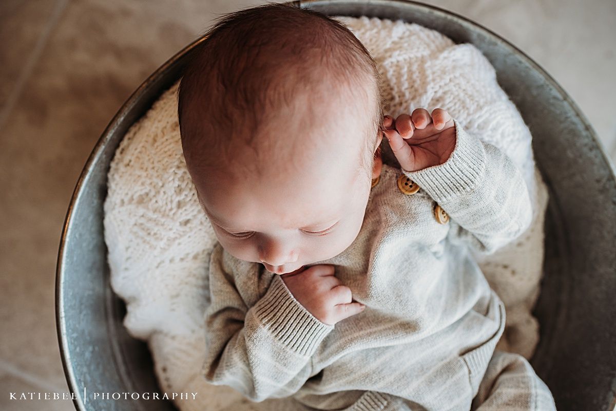 Overhead view of baby in white outfit resting in metal basin.