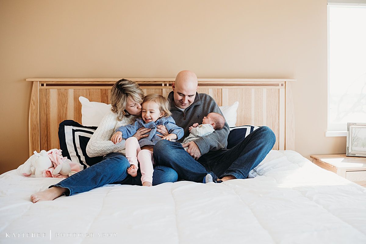 A family relaxes together on a wooden bed frame while bonding with their newborn.