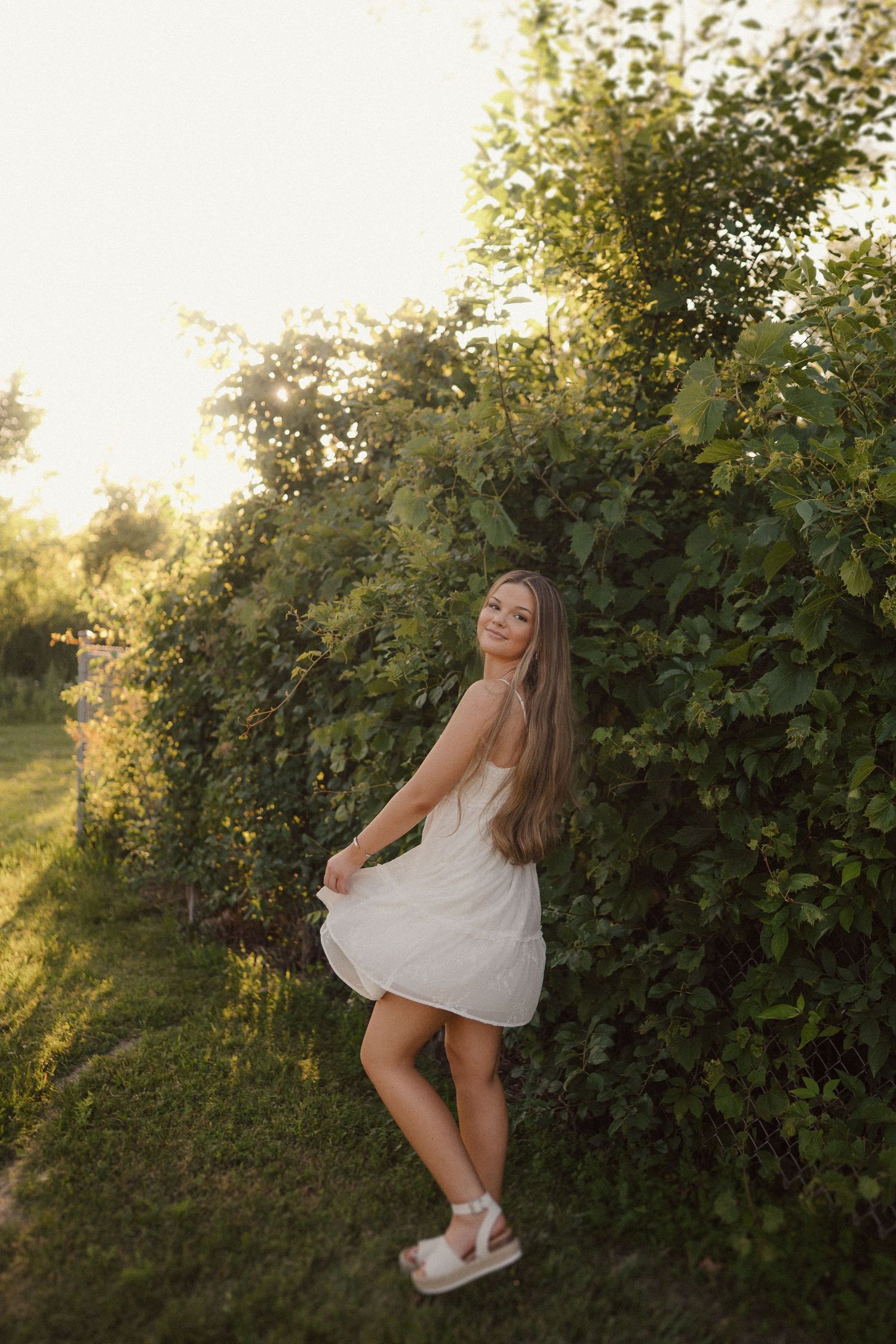 Outdoor summer photoshoot against a backdrop of green vines and foliage in warm evening light.