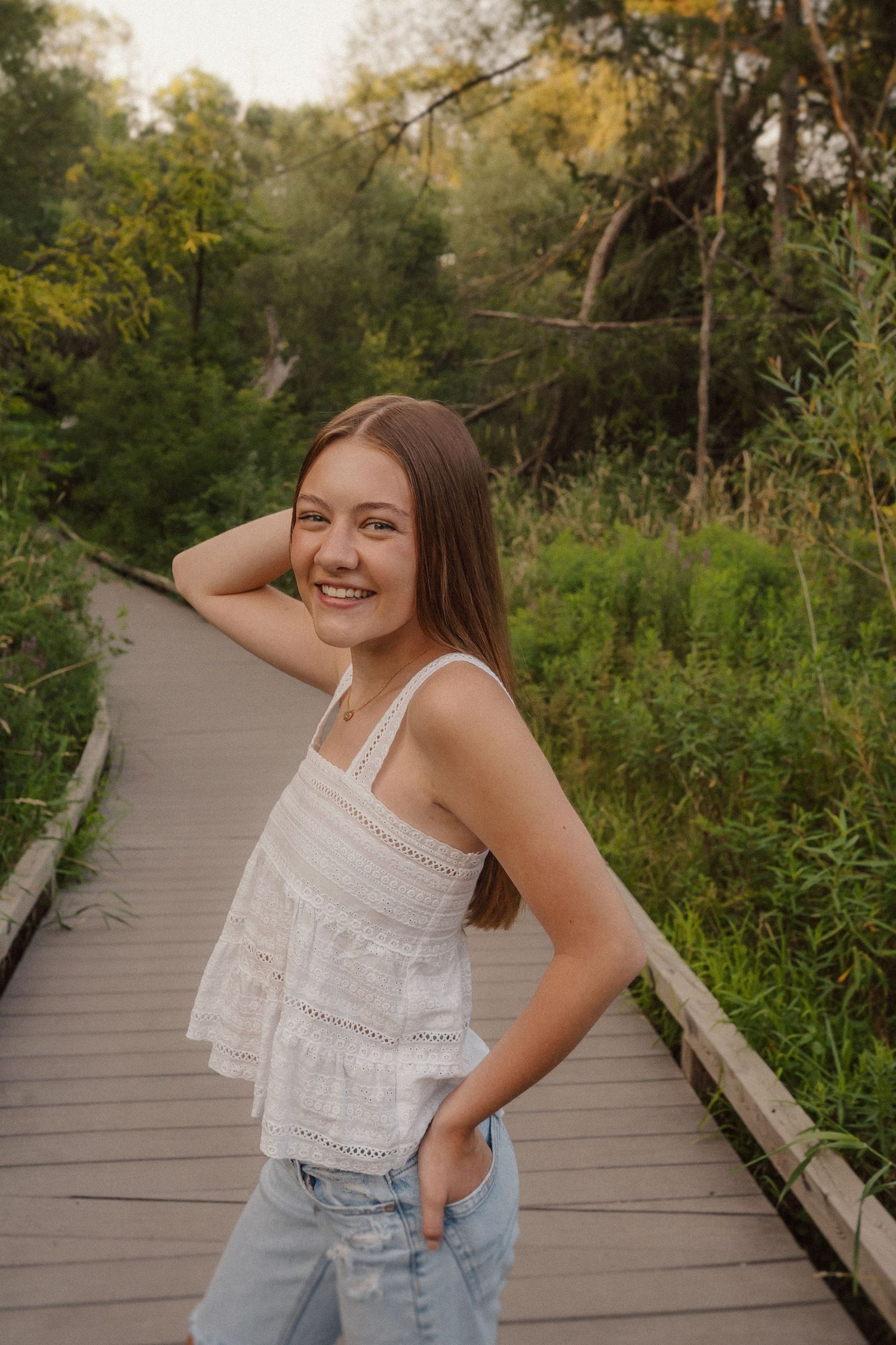 Candid outdoor photo on a wooden boardwalk surrounded by summer greenery at sunset.
