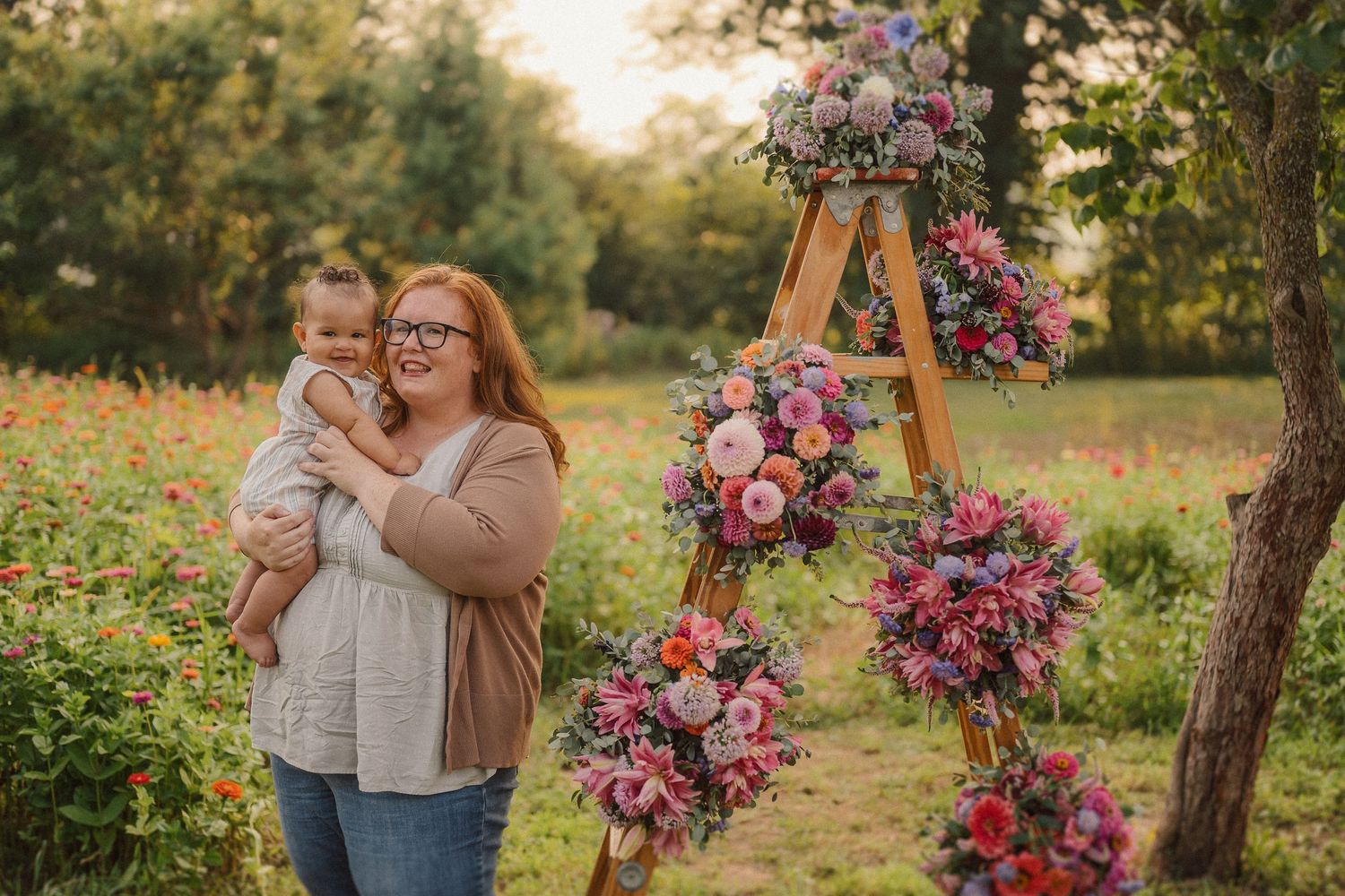 A tender moment shared outdoors next to a wooden ladder decorated with beautiful pink and purple floral arrangements.