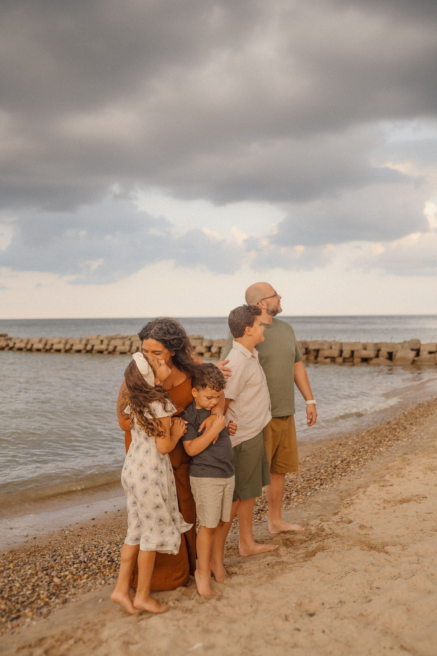 Candid family moments captured along a rocky beachfront with stormy clouds overhead.
