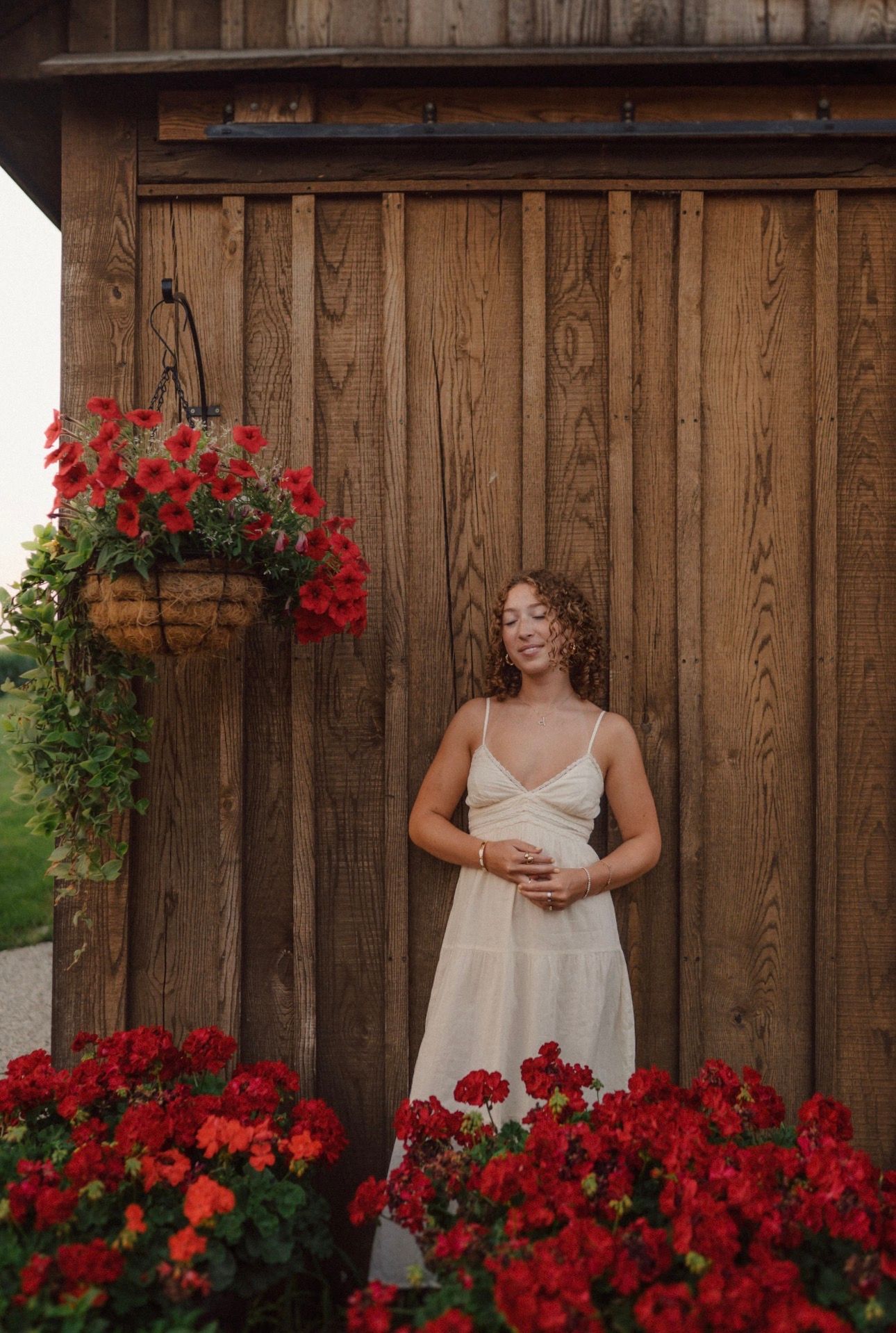 A romantic portrait against a wooden barn wall with bright red flowering plants.