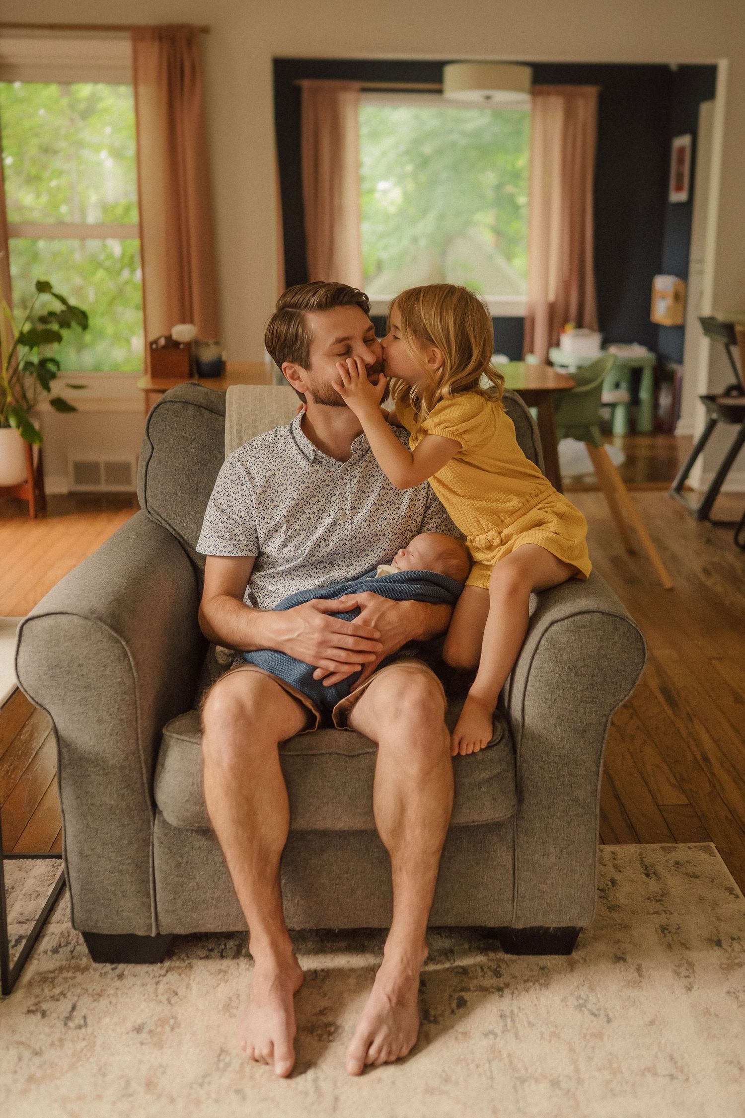 Warm sunlit images showing tender moments on a gray sofa with wooden floors and cream carpet.