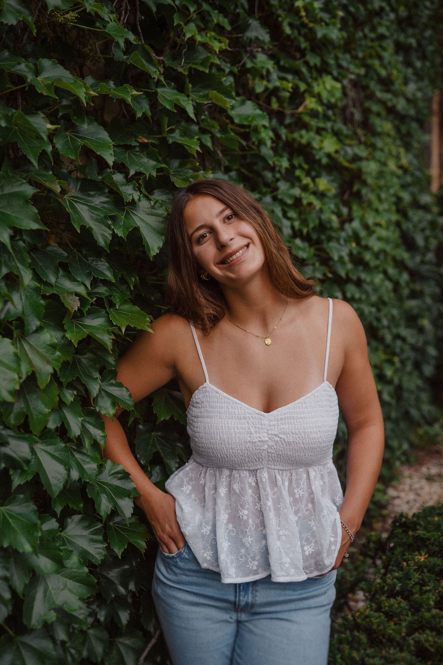 Summer portrait session against ivy-covered wall featuring white lace top and denim.