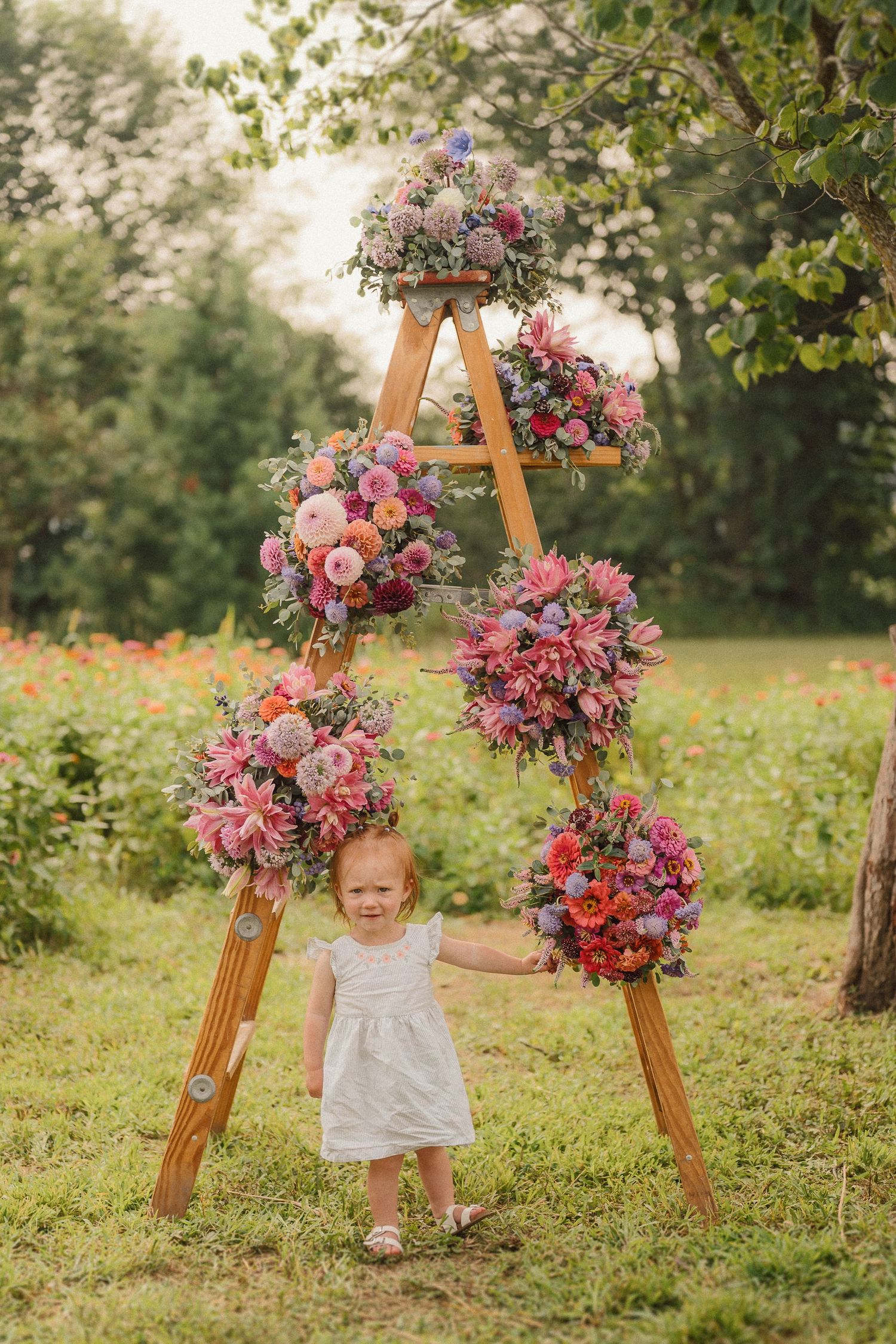 A wooden A-frame display adorned with vibrant pink and purple floral arrangements in a sunny garden setting.