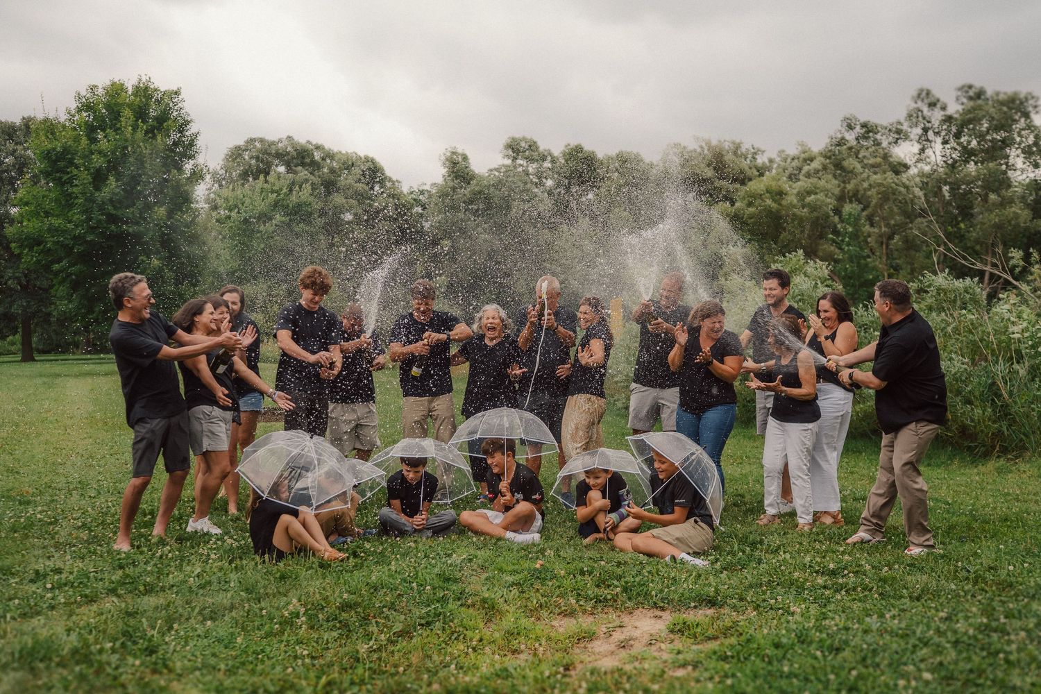 Large family group poses playfully in a field during cloudy outdoor photo session.