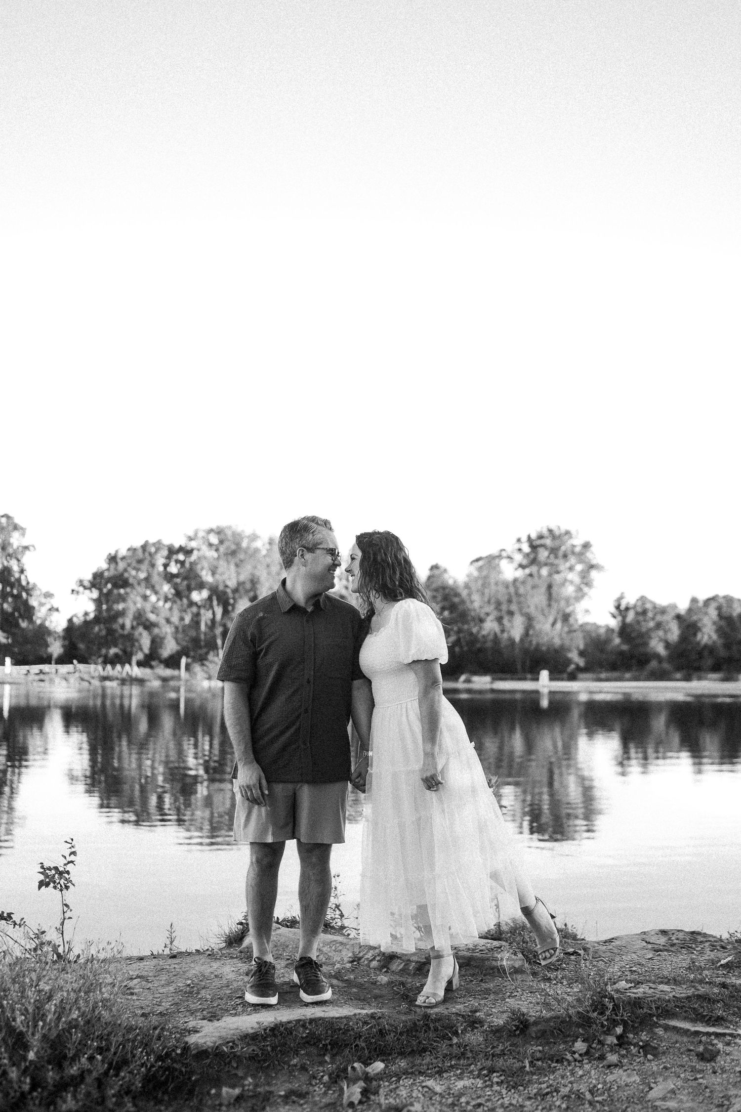 Black and white portrait of a couple sharing an intimate moment by a lake.