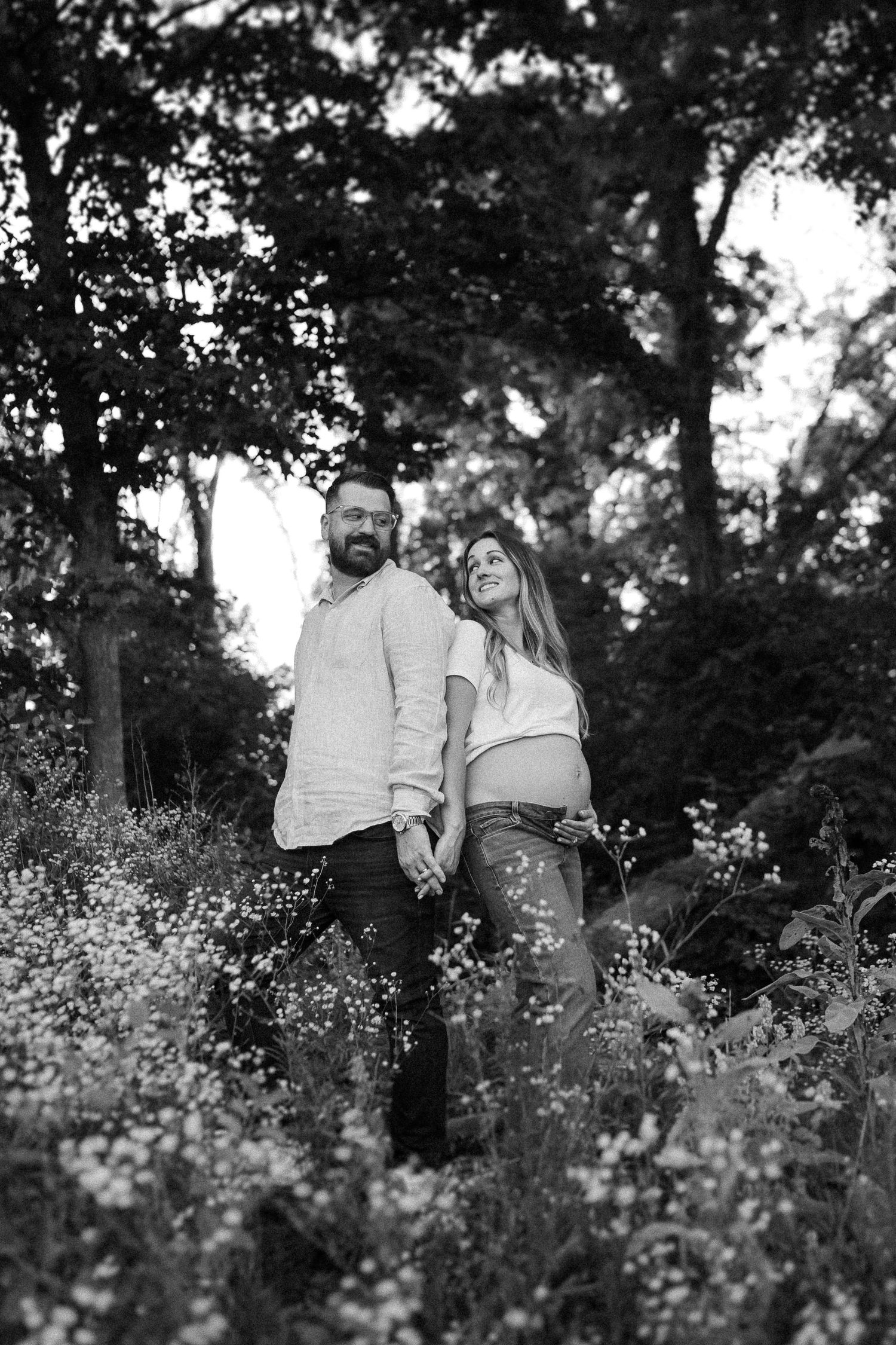 Black and white portrait of couple standing among wildflowers in a wooded setting.