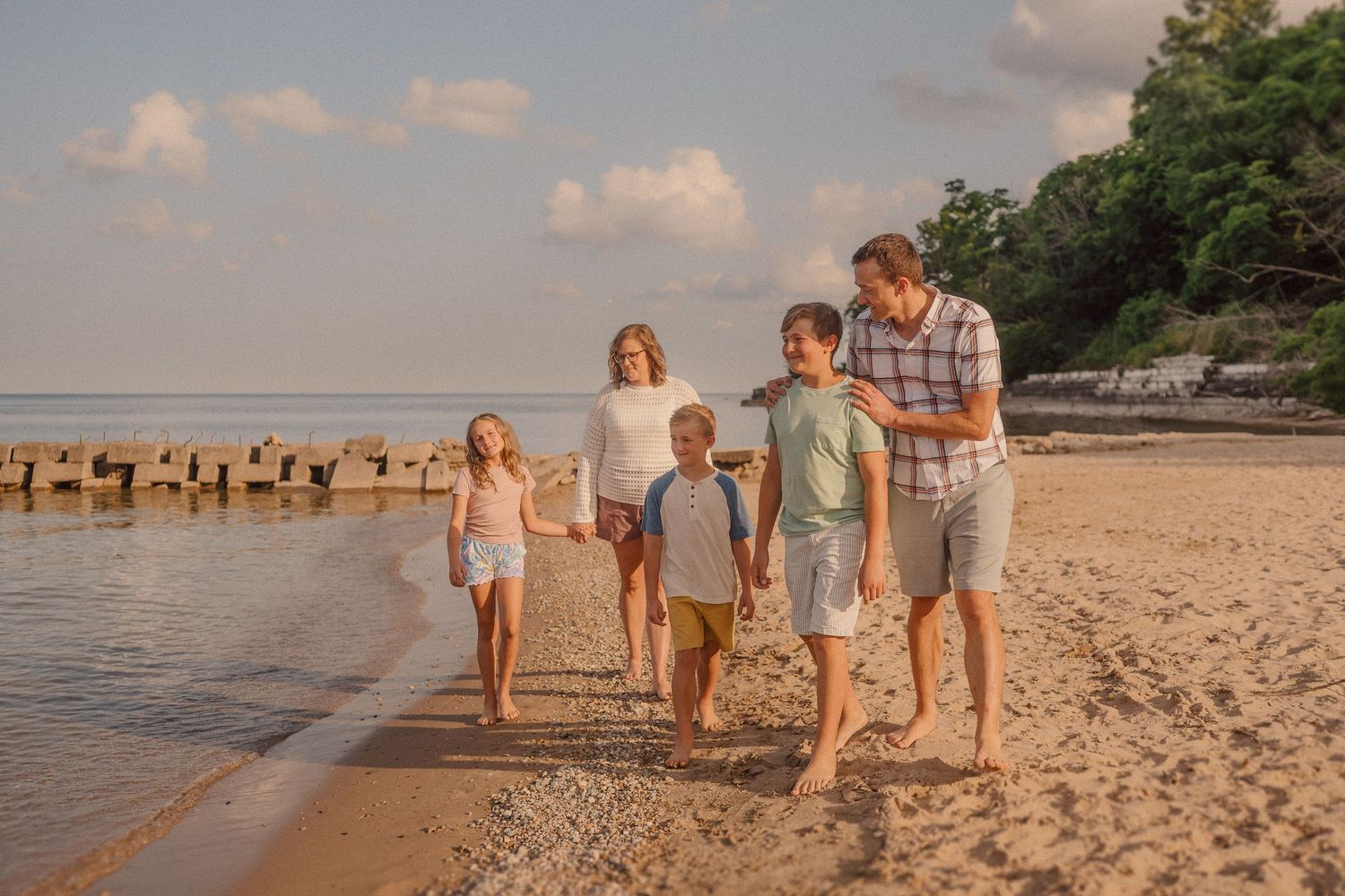 A small group enjoys a peaceful afternoon stroll along a scenic sandy beach at sunset.
