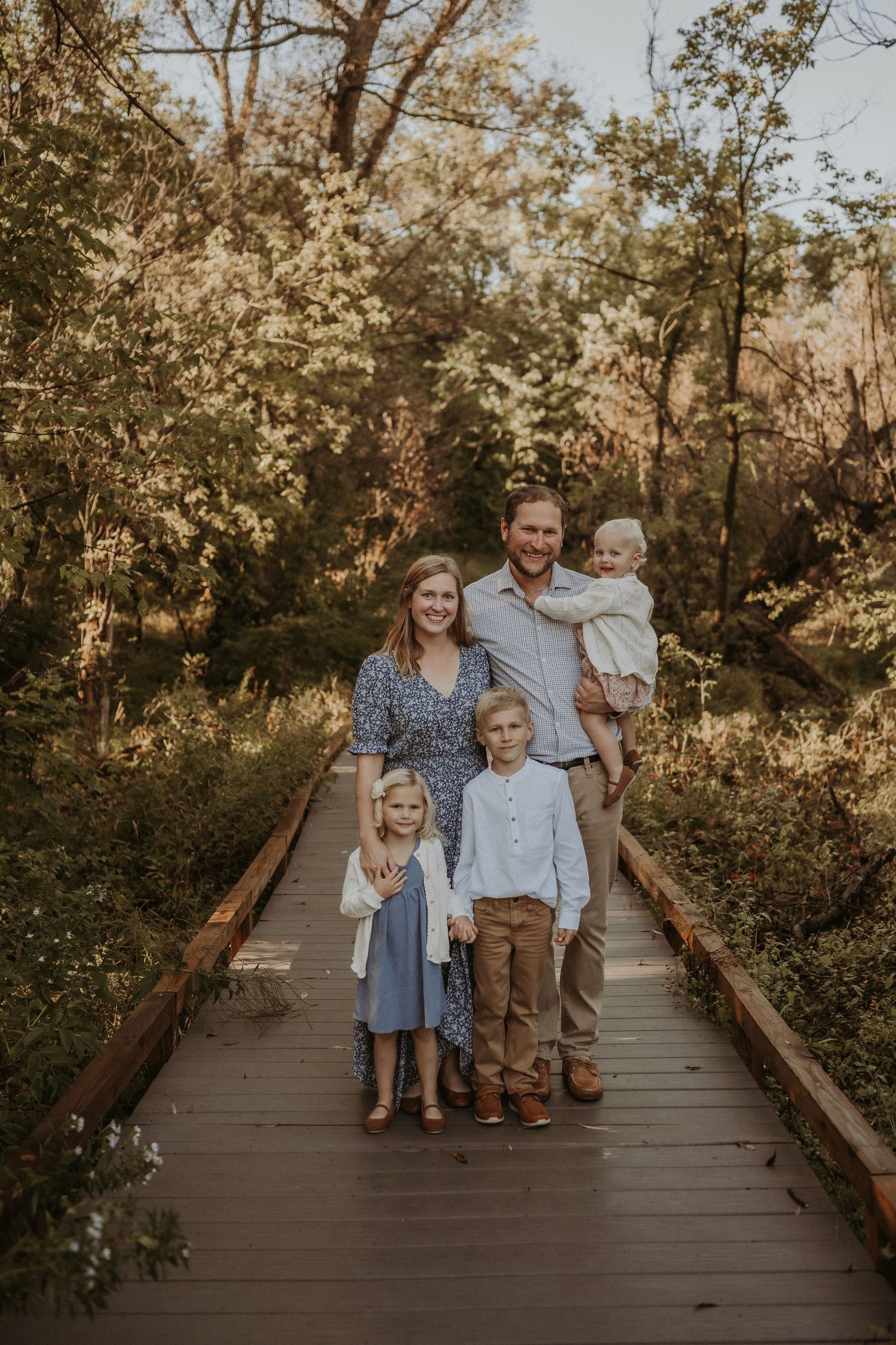 A family portrait on a wooden boardwalk surrounded by autumn trees.
