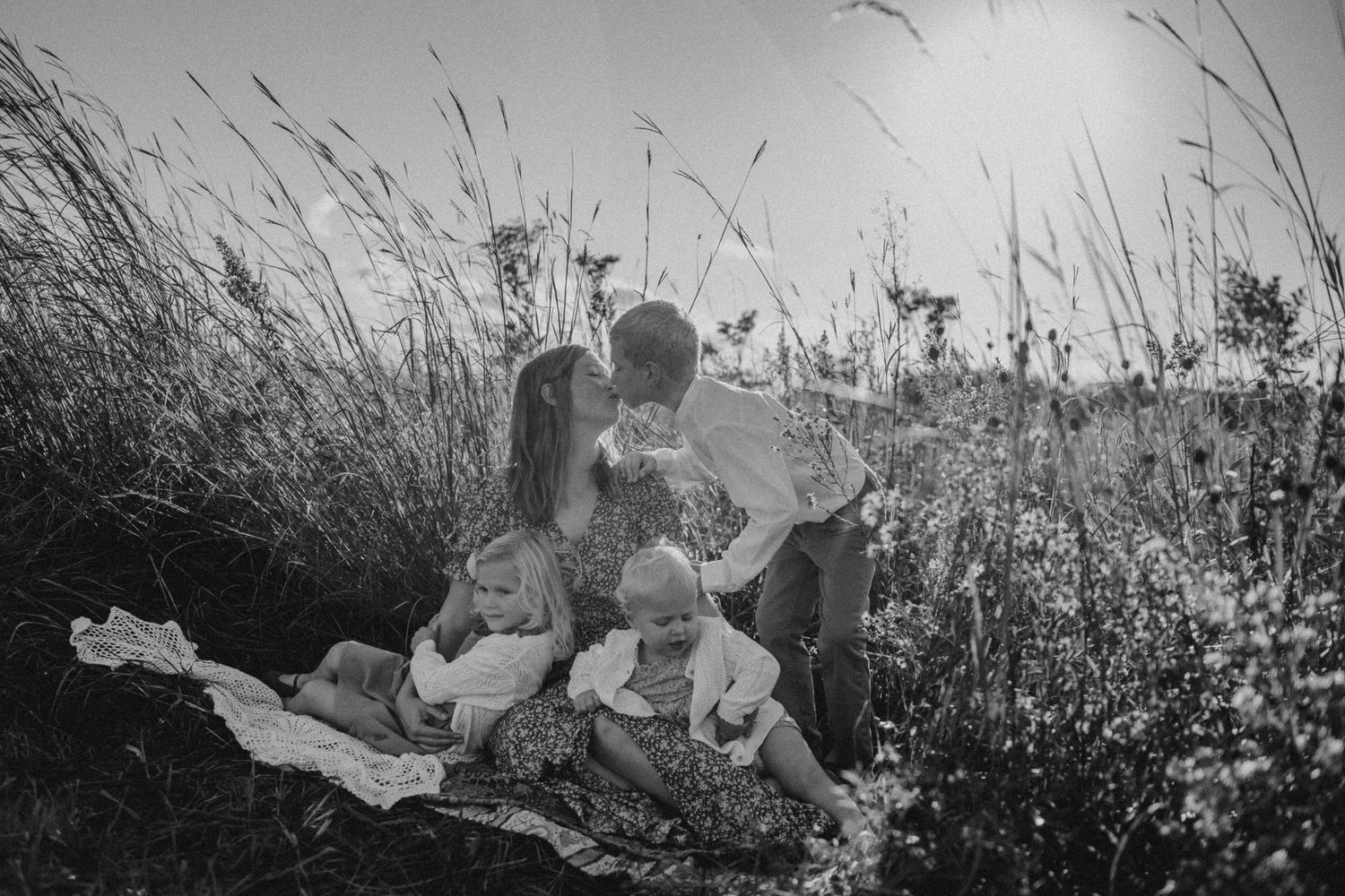 Black and white portrait of family sitting on blanket in tall grass meadow.