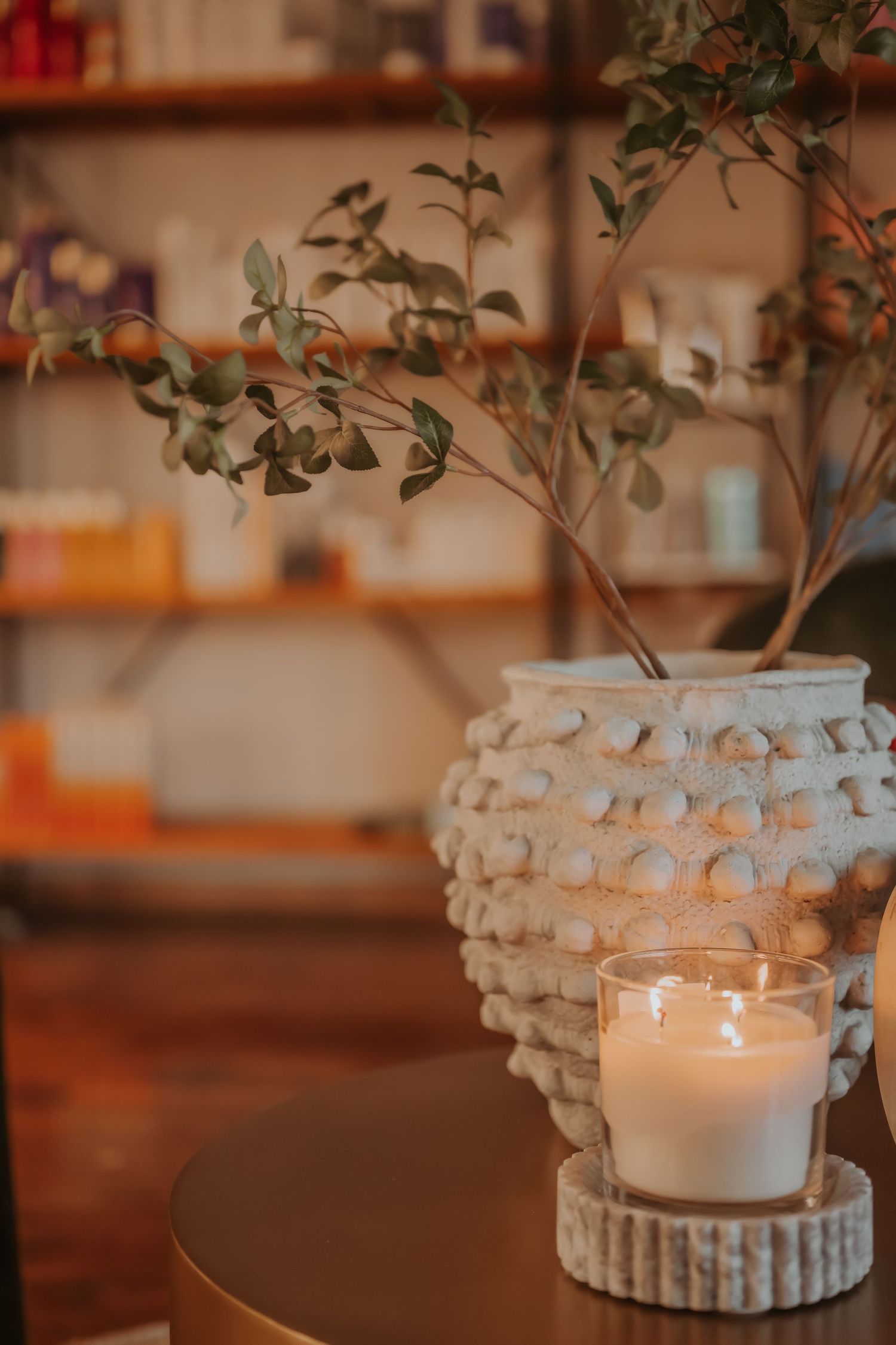 Close-up of textured white vase with eucalyptus stems and lit candle creating cozy ambiance.