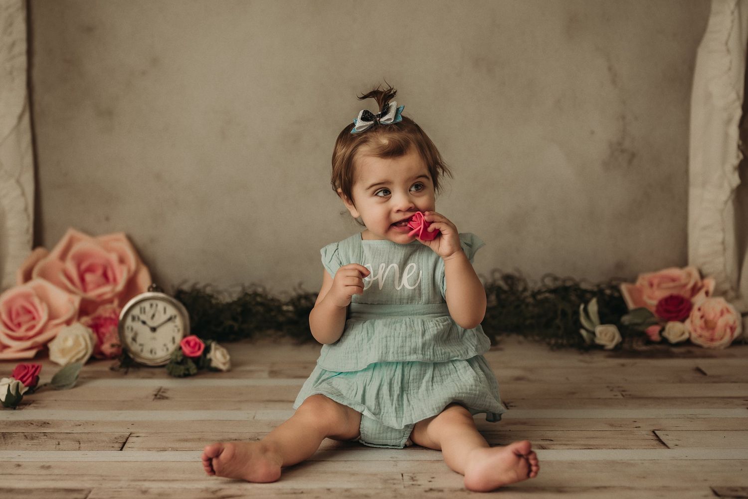 A vintage-styled portrait featuring a mint green dress, pink roses, and an antique clock on wooden flooring.