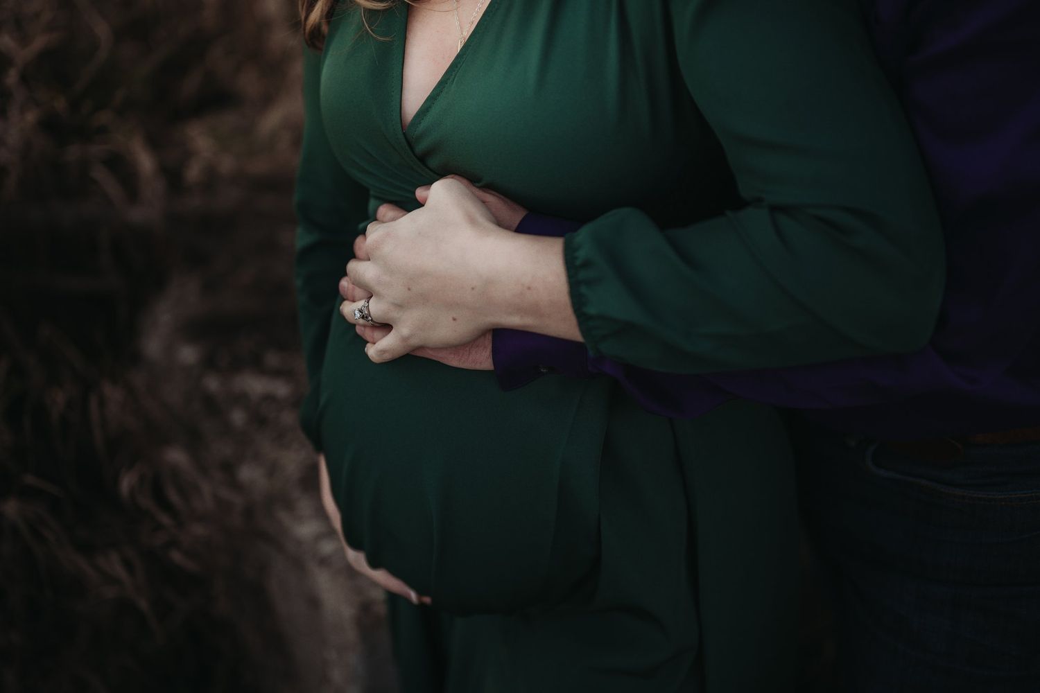 Close-up shot of hands tenderly cradling a pregnant belly in a green dress.