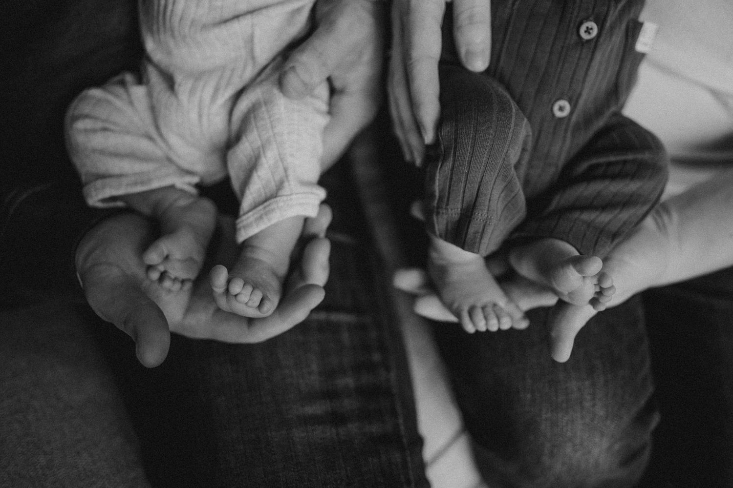 Close up black and white photo showing tiny baby feet next to adult hands.