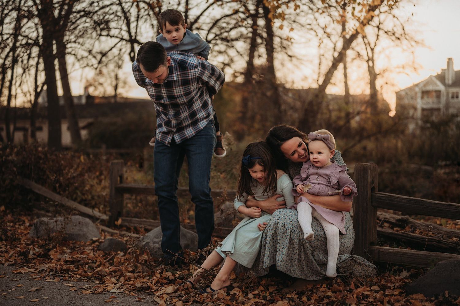 A family relaxes together on wooden steps surrounded by autumn foliage at sunset.