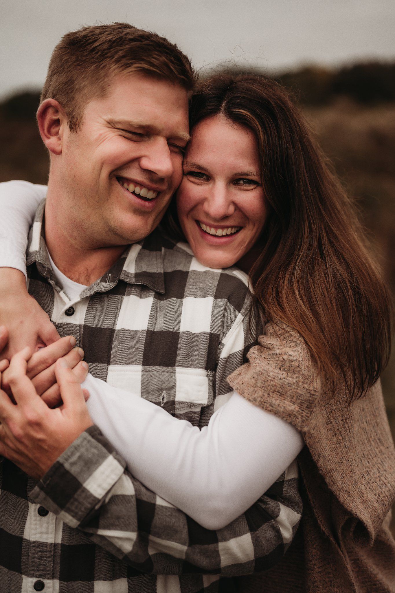 An intimate candid moment of a couple laughing and embracing in casual fall attire.