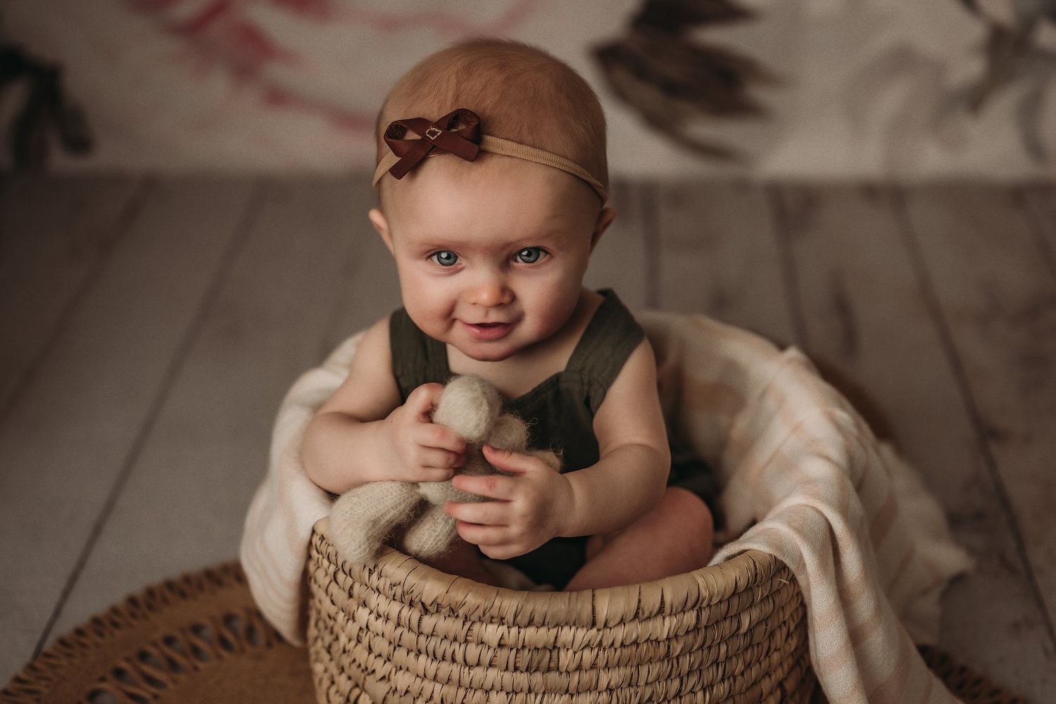 Young child seated in woven basket wearing green outfit and holding plush toy.