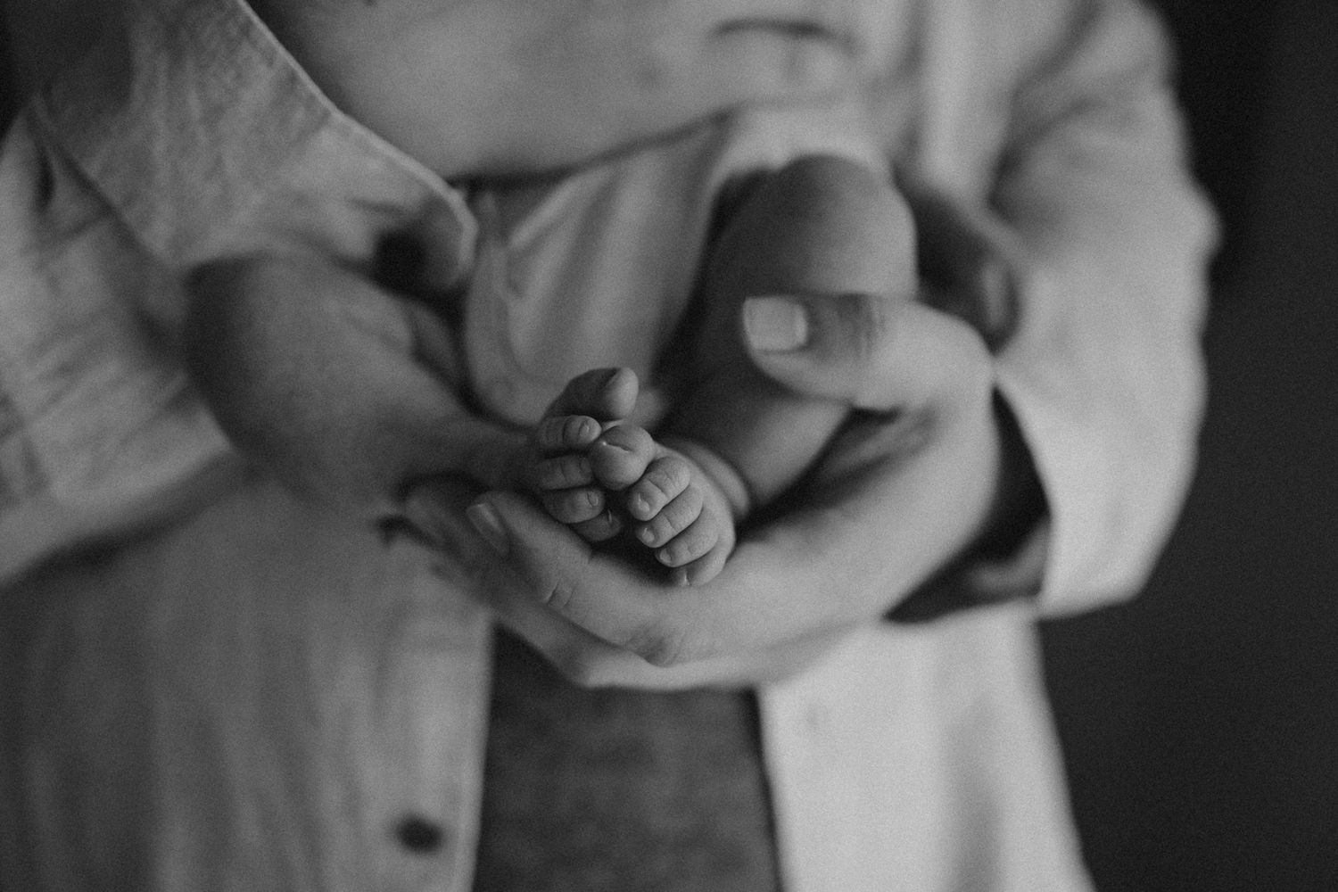 Black and white detail shot of tiny newborn feet being held in gentle hands.