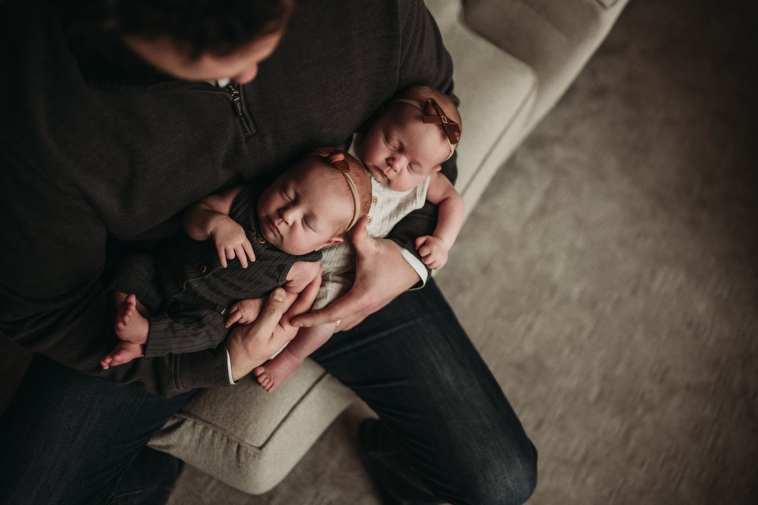 Overhead view of parent sitting with active newborn baby on light colored couch.