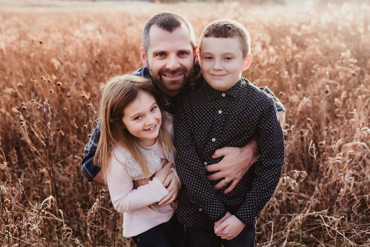 Family portrait with three people hugging close together in a golden field.