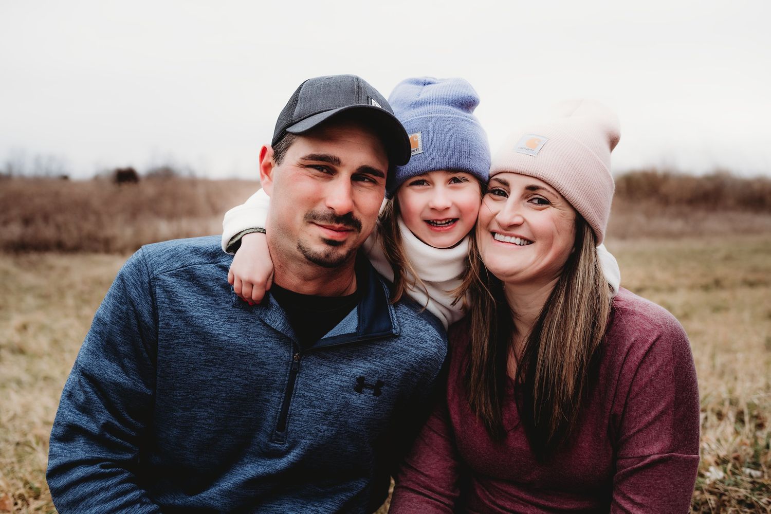 Close-up portrait of family wearing winter hats and warm clothing outdoors.