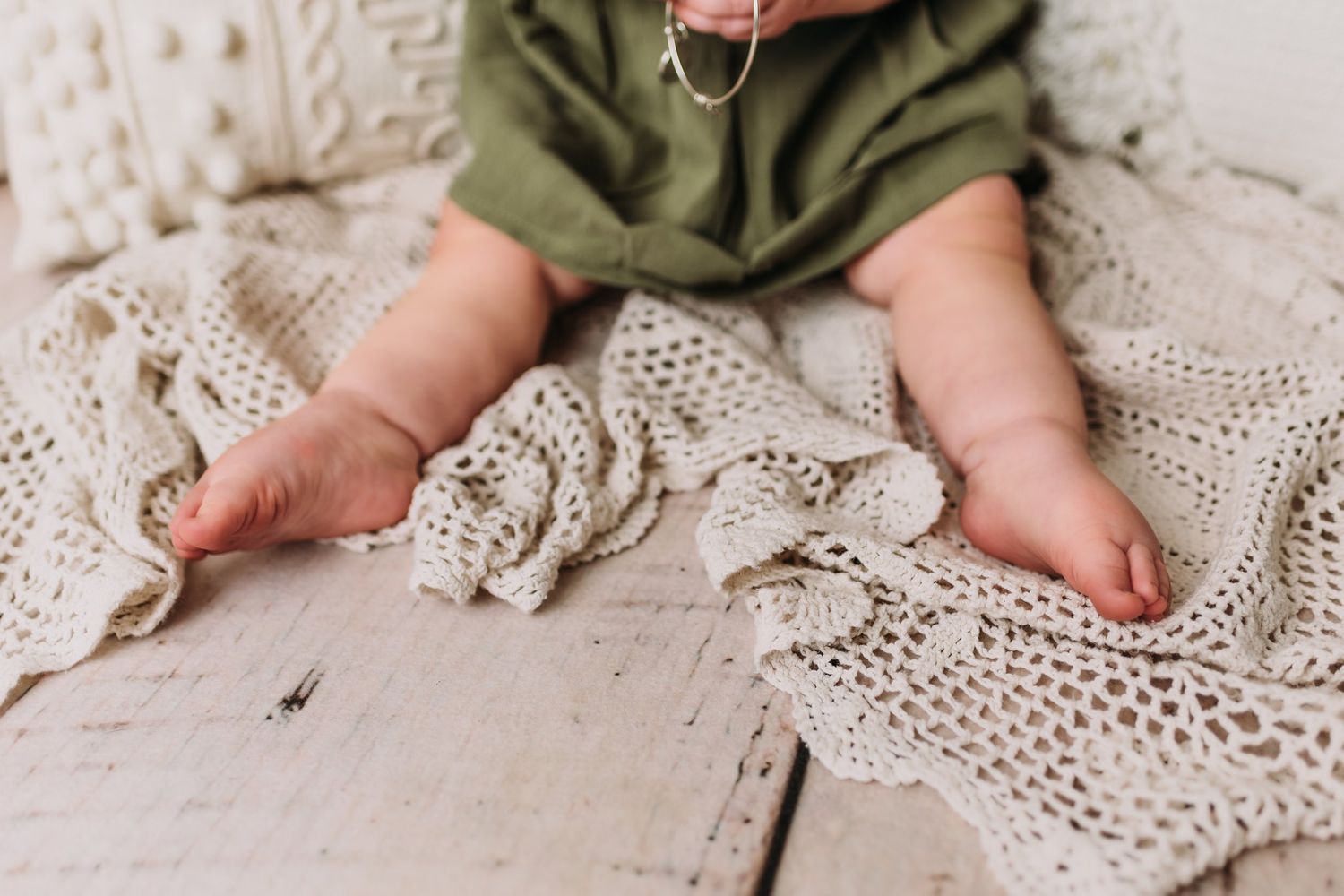Tiny bare feet rest on vintage lace blanket against wooden floor.