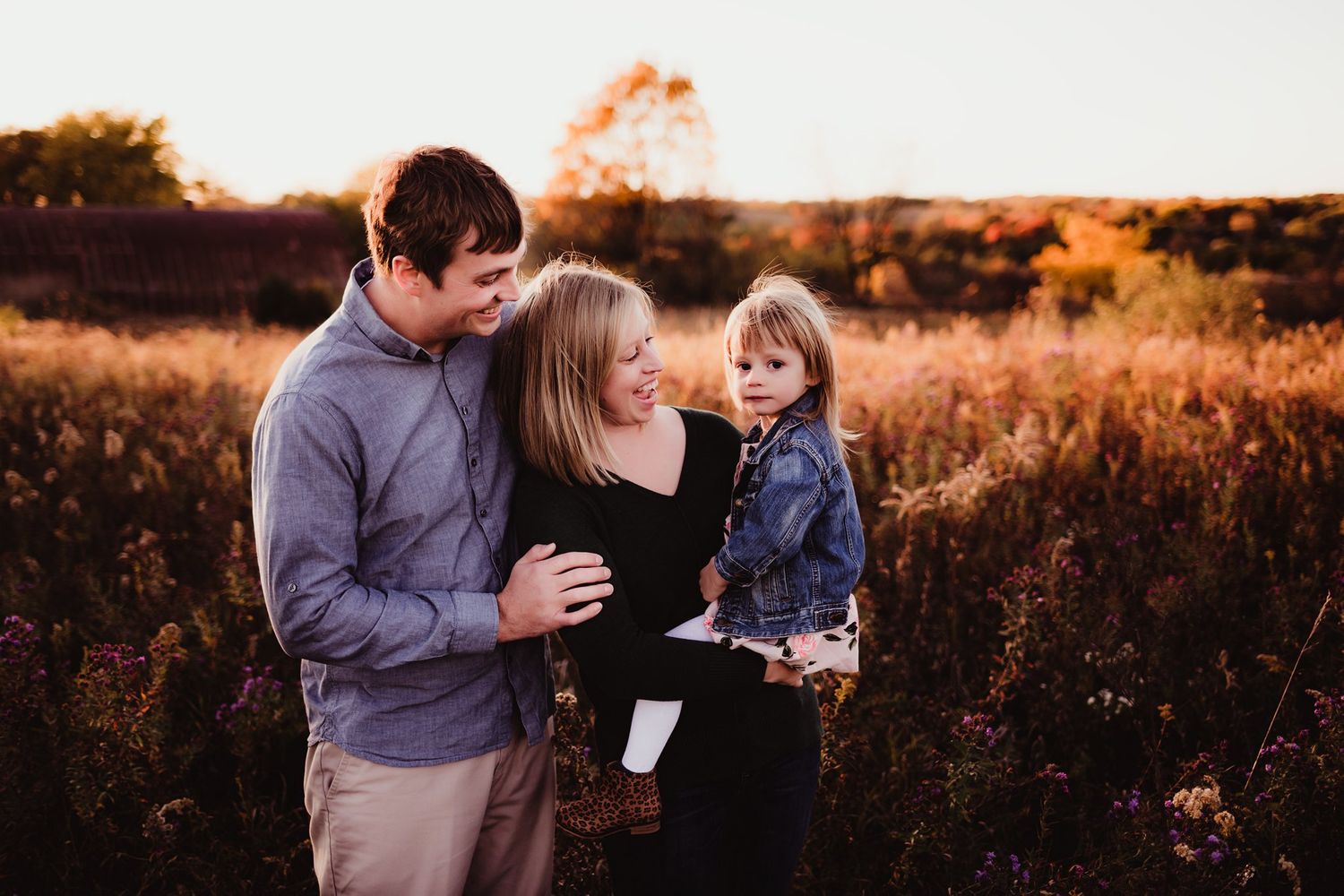 A tender family moment captured in golden evening light with a rustic barn in the distance.